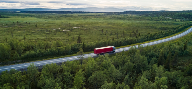 Lastbil kör på enslig väg genom ett norrländskt landskap.
