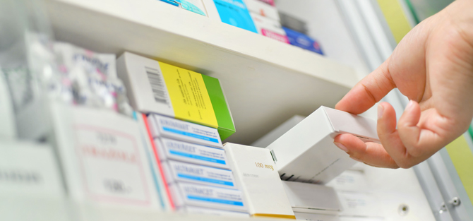 Close-up of hand taking a box from a shelf filled with various medicines.