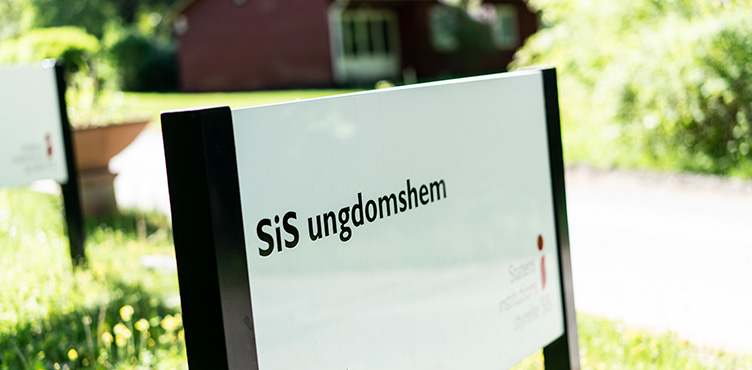 Närbild på skylt med texten "SiS ungdomshem". Man ser även logotypen för Statens institutionsstyrelse lite svagt i nedre högra hörnet.